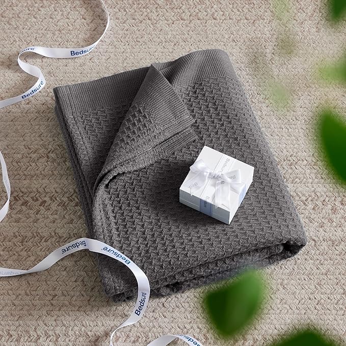 Folded gray textured blanket with a white block of soap on a beige carpet, branded 'Bedbath'.