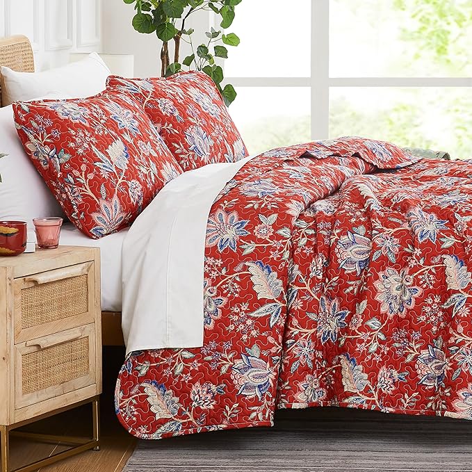 Red floral bedding set on a bed in a bright room with a wooden nightstand.