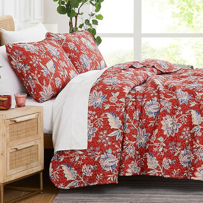 Red floral bedding set on a bed in a bright room with a wooden nightstand.