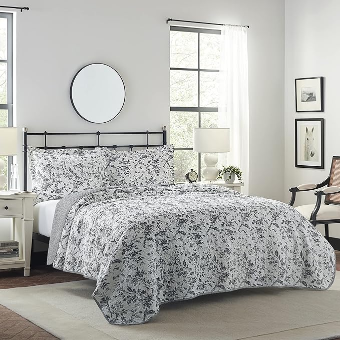 Floral bedding set on a bed in a bedroom with a mirror and lamp.