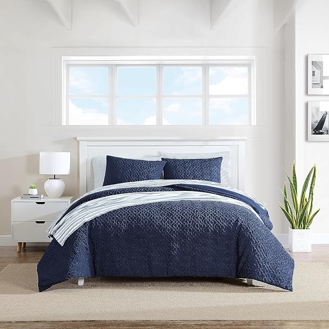 Navy blue quilt set on a bed in a bright bedroom with a window and nightstand.