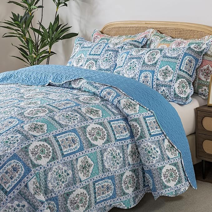 Patterned quilt and pillows on a bed with a plant in the corner