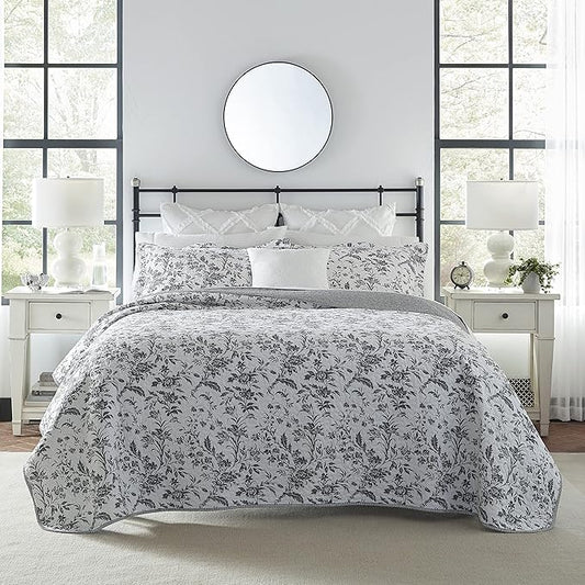 Bed with floral patterned comforter in a bedroom setting with two nightstands and lamps.