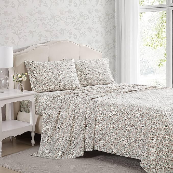 Floral patterned bedding set on a bed in a bedroom with a side table and lamp.
