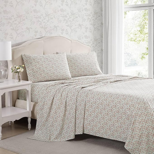 Floral patterned bedding set on a bed in a bedroom with a side table and lamp.